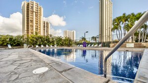 Una piscina con sillas de descanso, rodeada de edificios altos y palmeras.