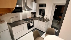 A modern kitchen with white cabinetry, a built-in oven, and a dining area with a table and chairs. - Delightful holiday home away from home, wetroom, UFH, garden/parking, local park (London)