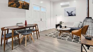 Un salon moderne avec un coin repas, comprenant un téléviseur fixé au mur, un canapé, une table basse et une cage à oiseaux décorative.