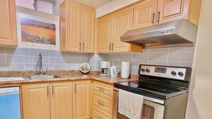 Una cocina con armarios de madera, una campana extractora de acero inoxidable, lavavajillas y un microondas empotrado.