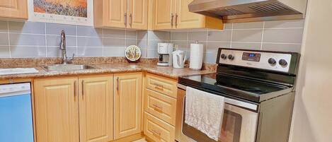 A kitchen with wooden cabinets, a stainless steel range hood, a dishwasher, and a wall-mounted microwave.