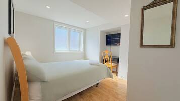Un dormitorio con cama, ventana, escritorio, silla, televisor y espejo.