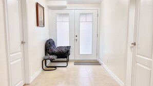 Un pasillo con dos puertas blancas, un banco y un cuadro en la pared.