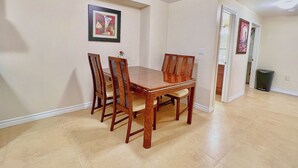 Un comedor con una mesa y sillas de madera, un cuadro enmarcado en la pared y un cubo de basura.