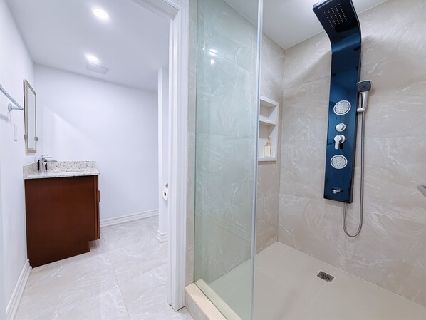 Un baño moderno con cabina de ducha de vidrio, suelo de baldosas de mármol y tocador de madera.