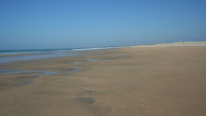 A wide sandy beach with gentle waves and a clear blue sky.