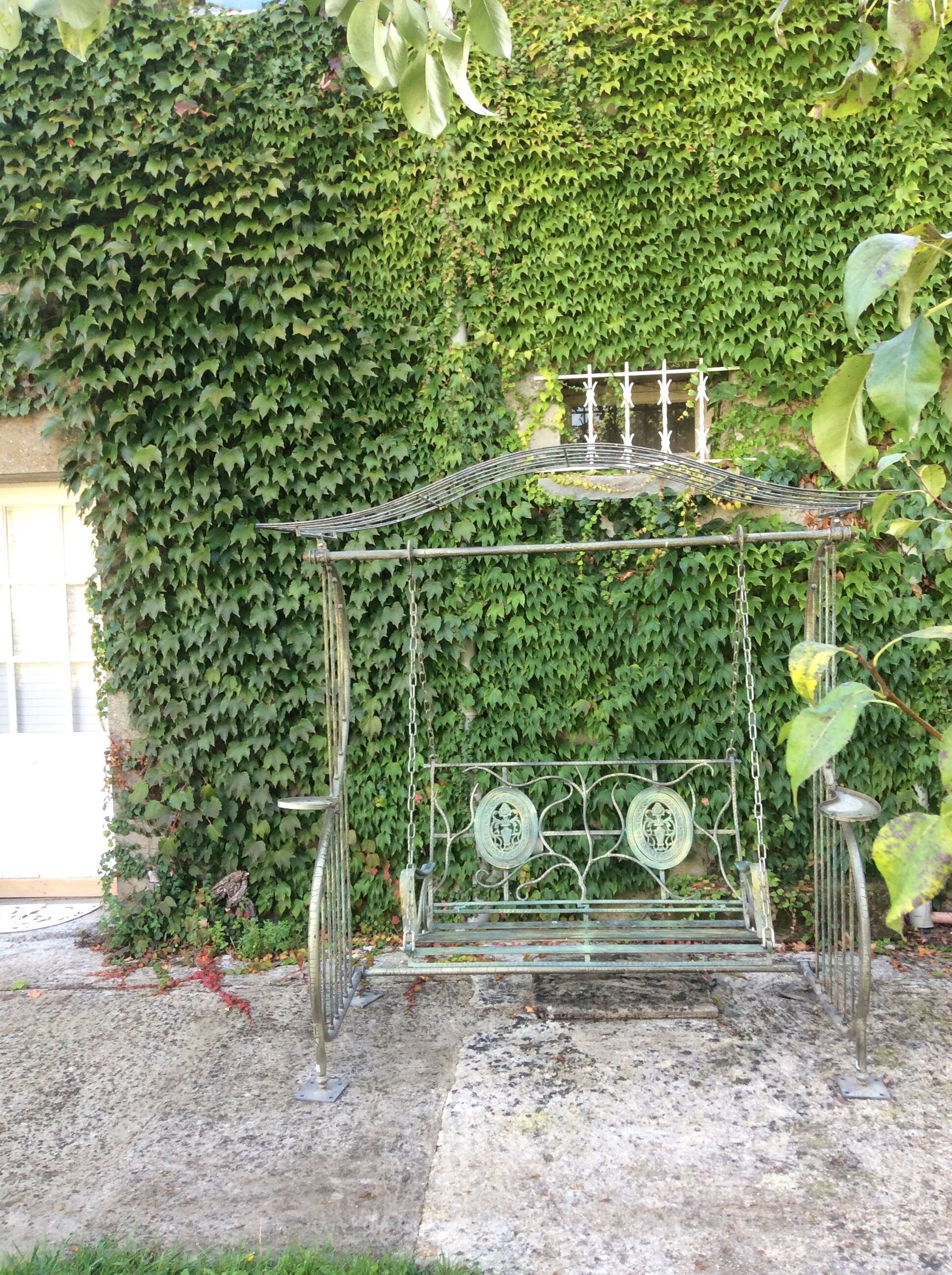A metal bench with a decorative backrest and two circular metal plates, set against a wall covered in green ivy.