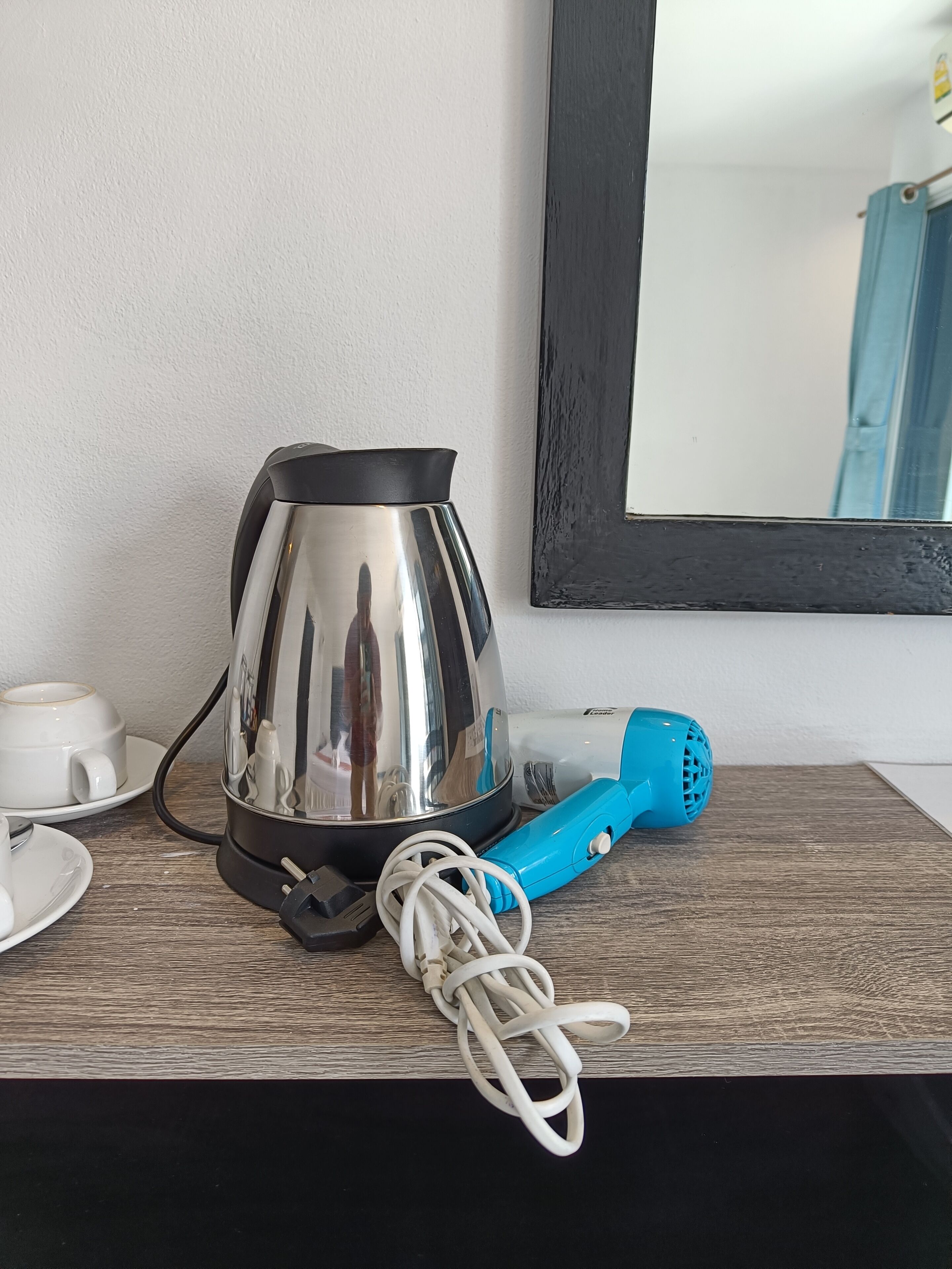 A kettle, a blue hairdryer, and a cup on a wooden surface.