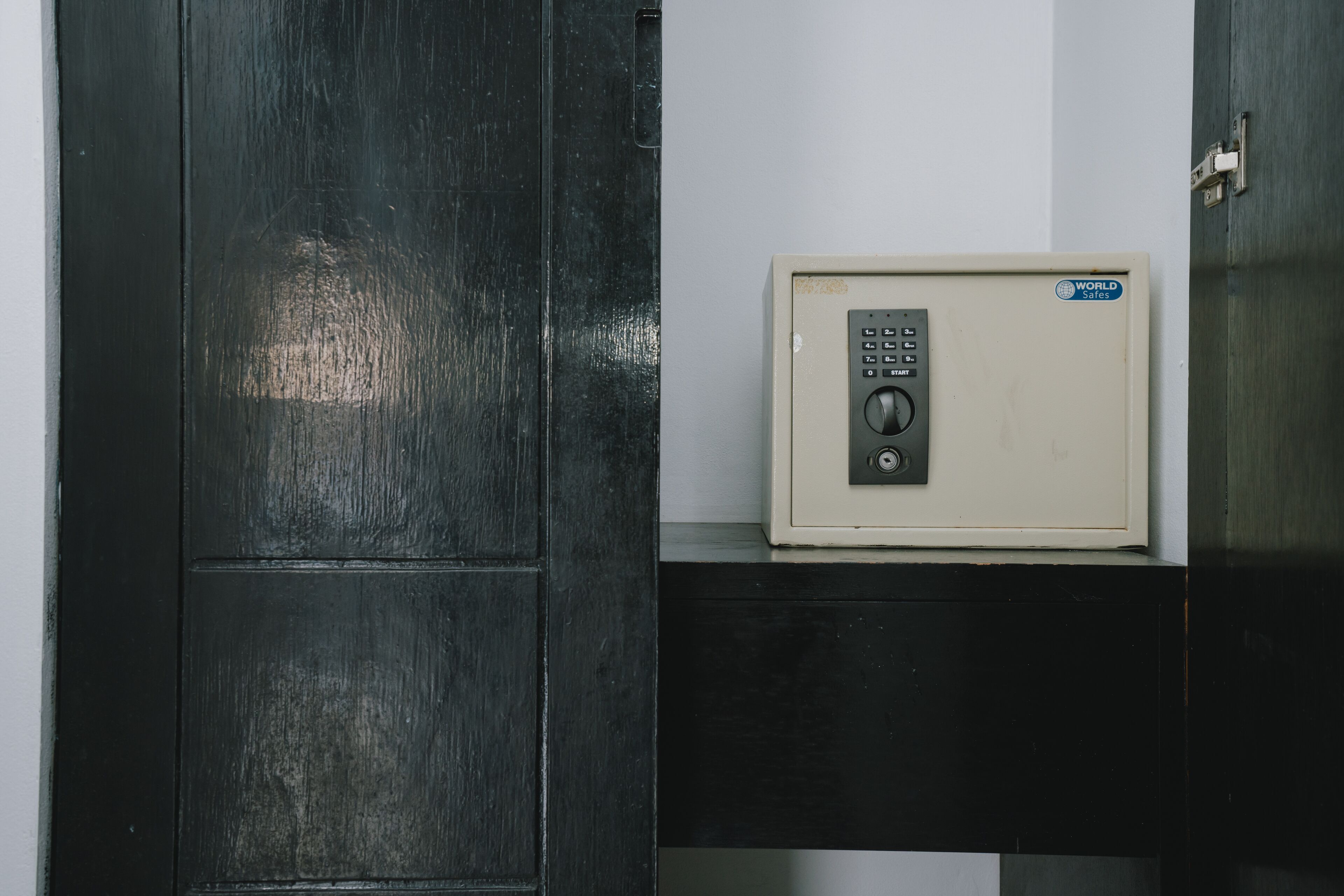 A secure safe with a keypad lock, placed on a black shelf against a white wall.