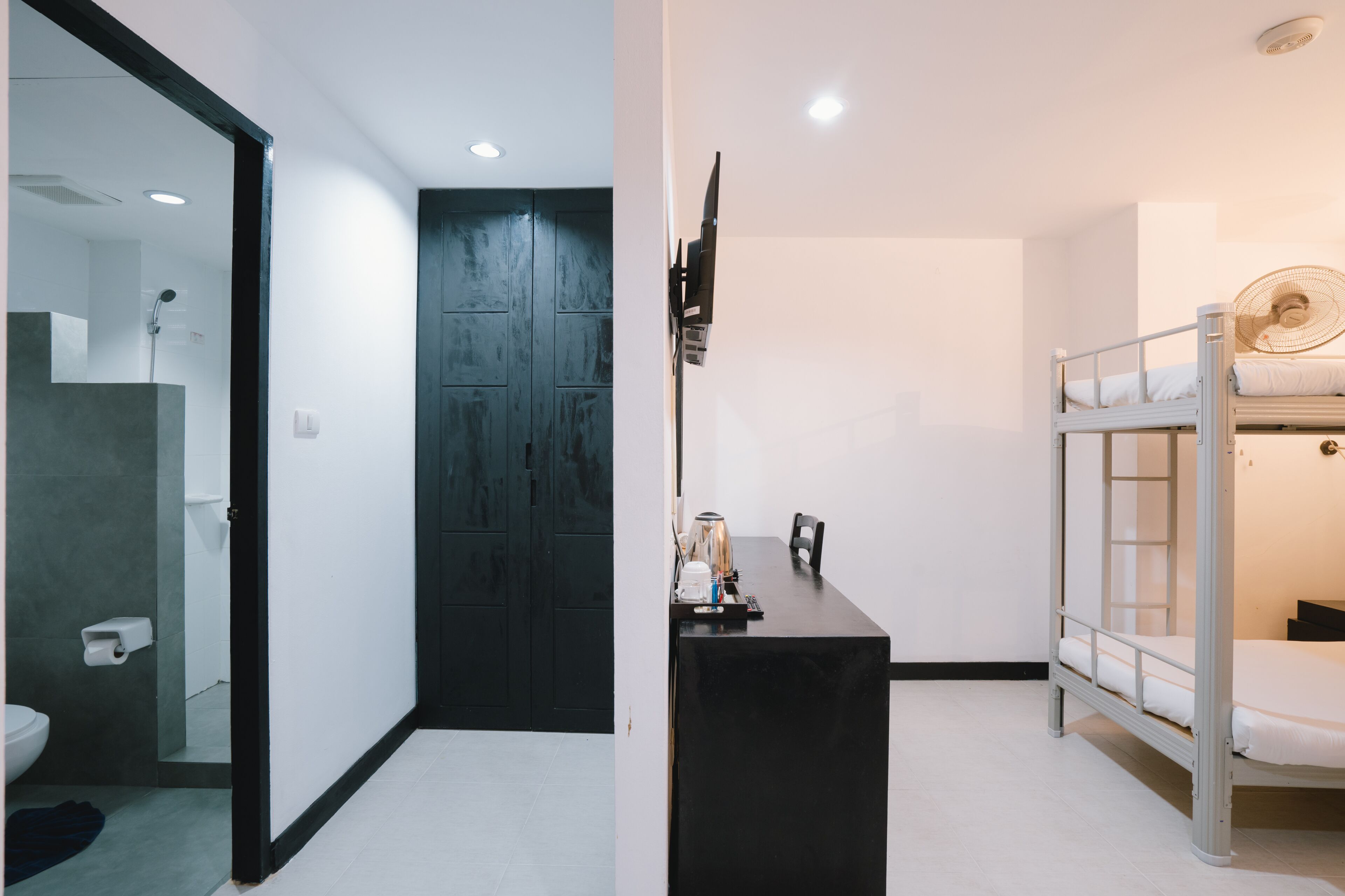 A modern room with a black door, a small table with a kettle, and a bunk bed with a fan.