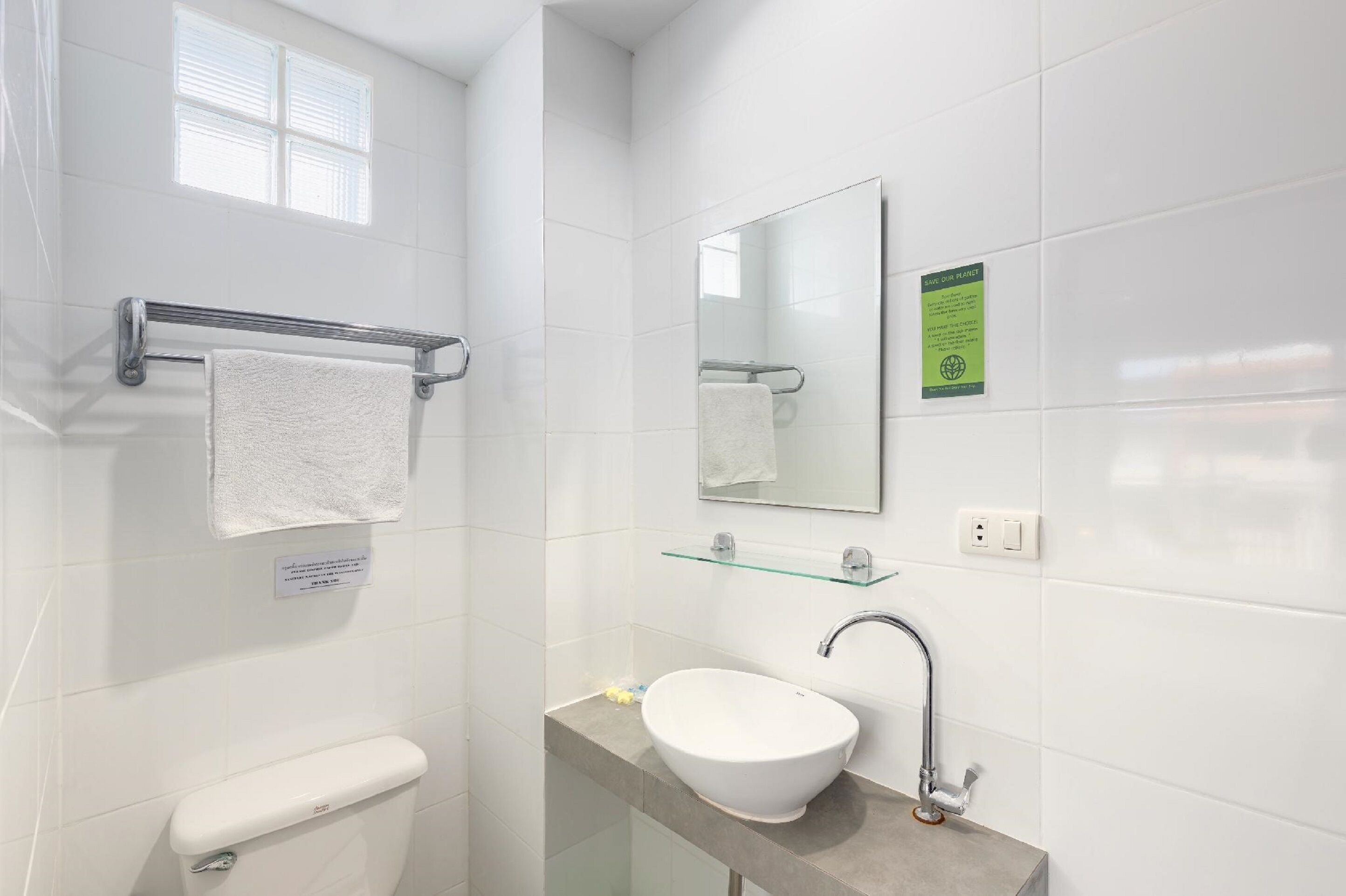 Un baño moderno con un inodoro blanco, un estante de vidrio sobre el lavamanos y un espejo con un letrero verde.