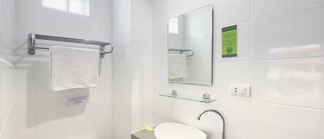 Un baño moderno con un inodoro blanco, un estante de vidrio sobre el lavamanos y un espejo con un letrero verde.