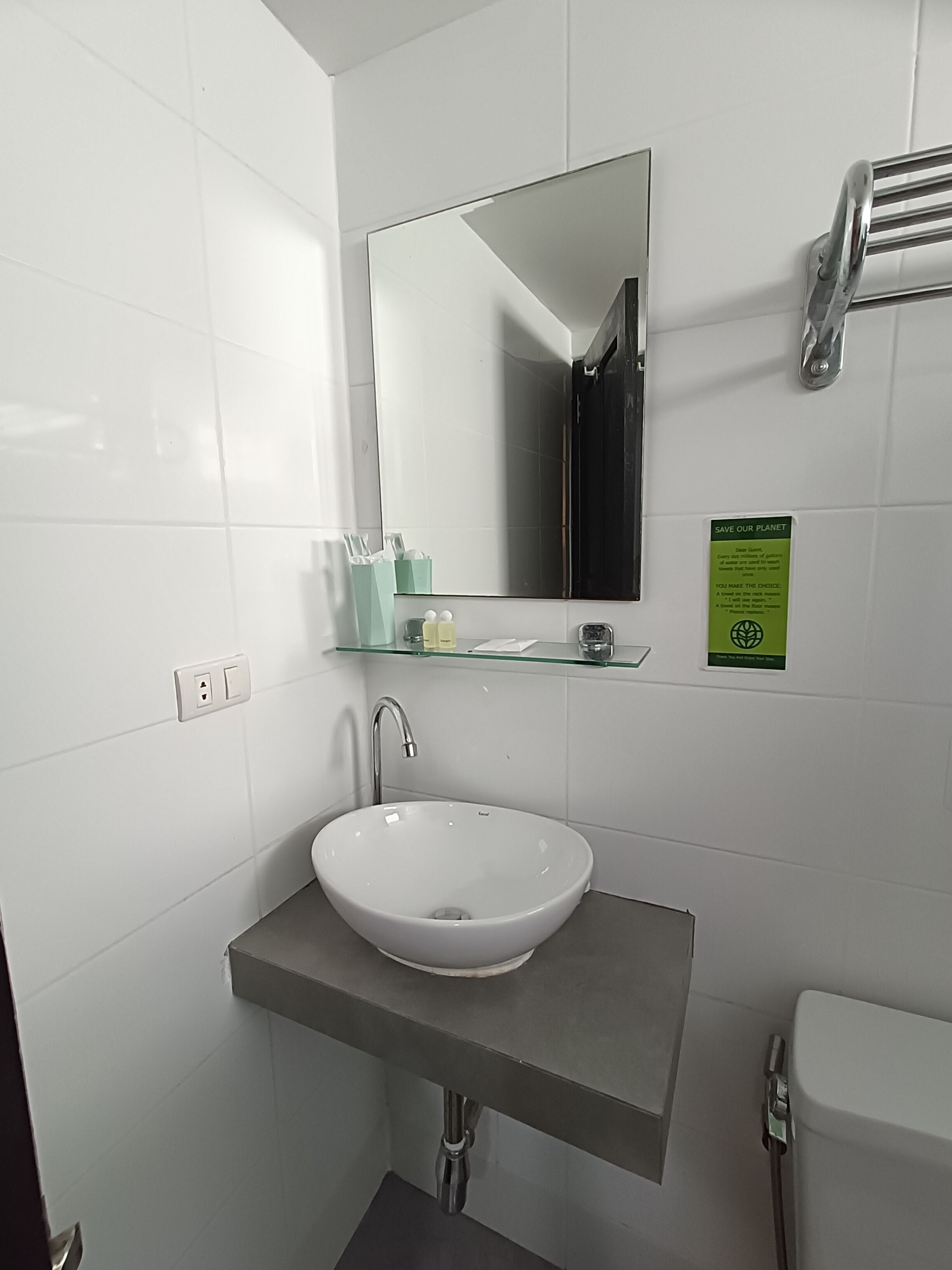 A modern bathroom with a white sink, a mirror, and a glass shelf with toiletries.