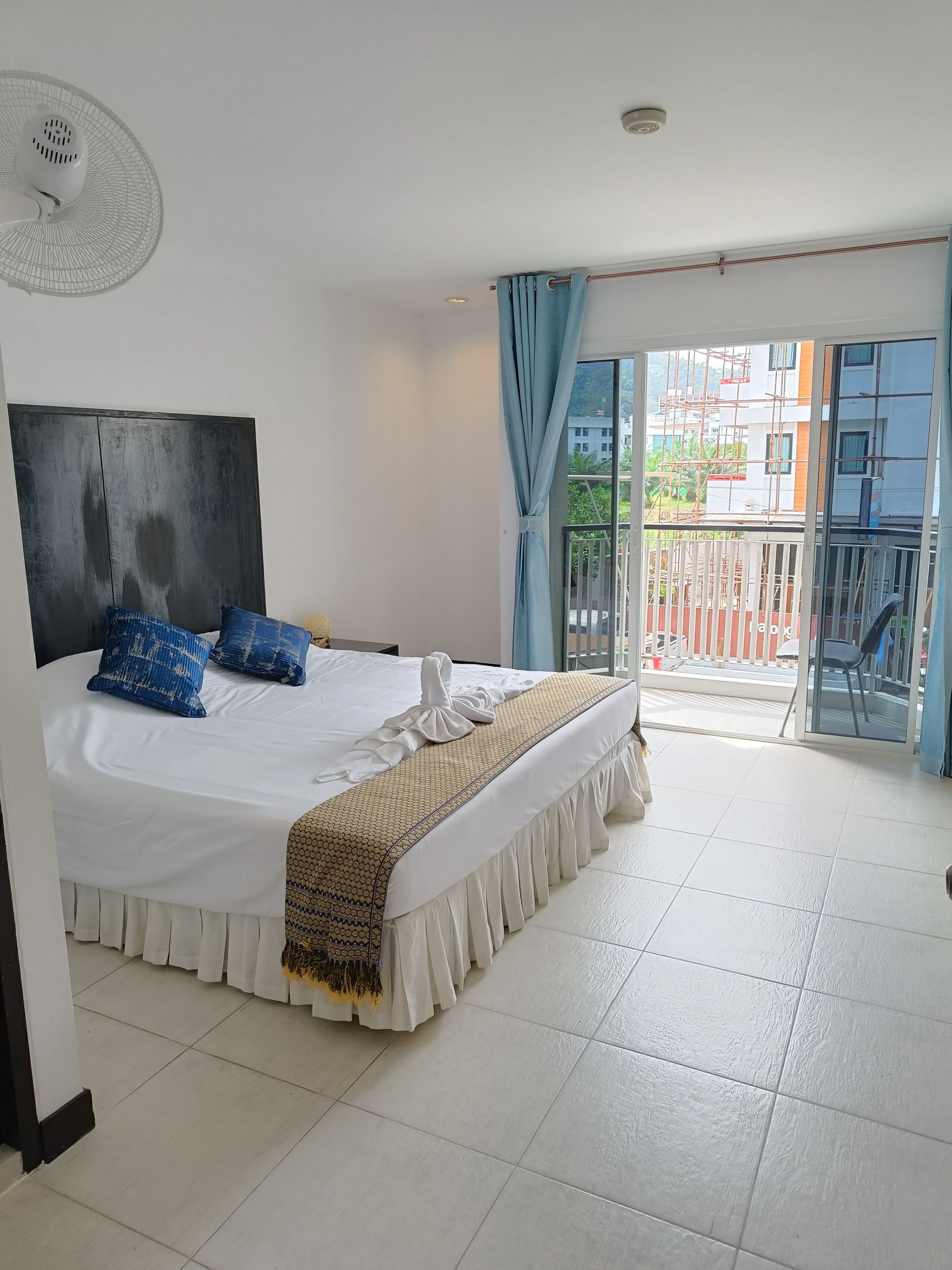 A hotel room with a large bed, a ceiling fan, and a view of the outside balcony.