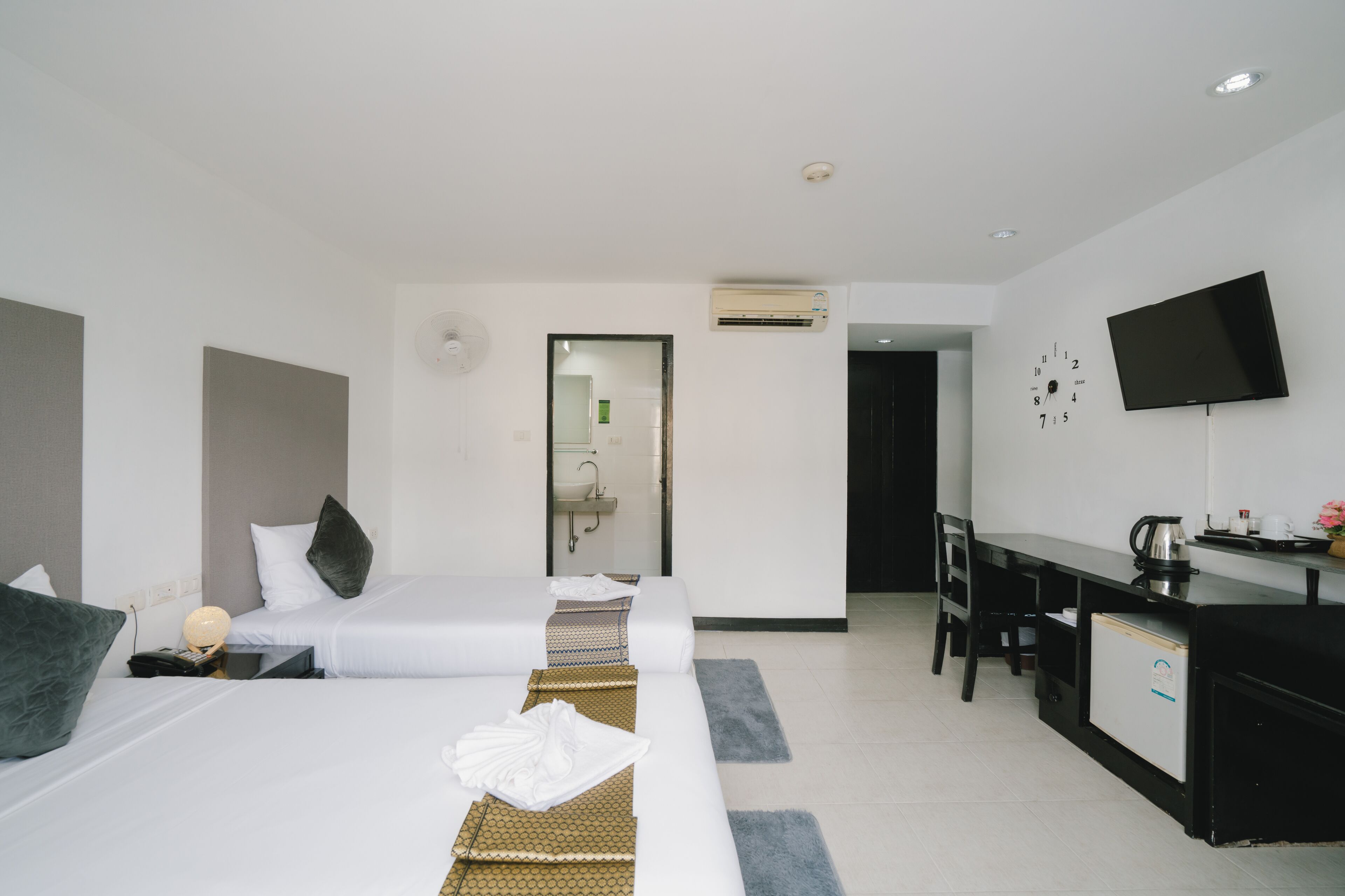 A hotel room with two beds, a desk, a TV, and a bathroom visible through an open door.