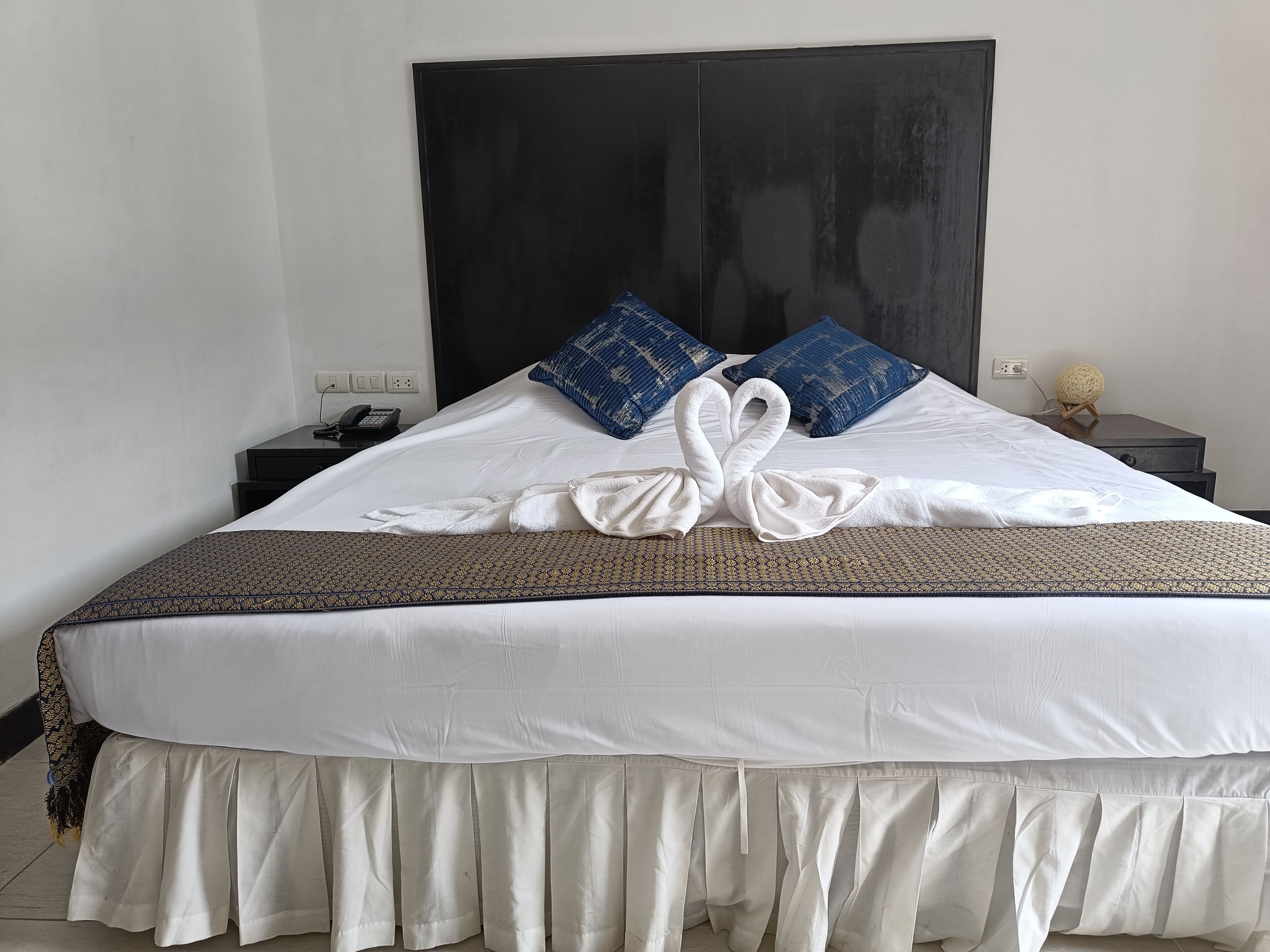 Una cama bien hecha con una colcha blanca, una decoración de toallas y almohadas azules.