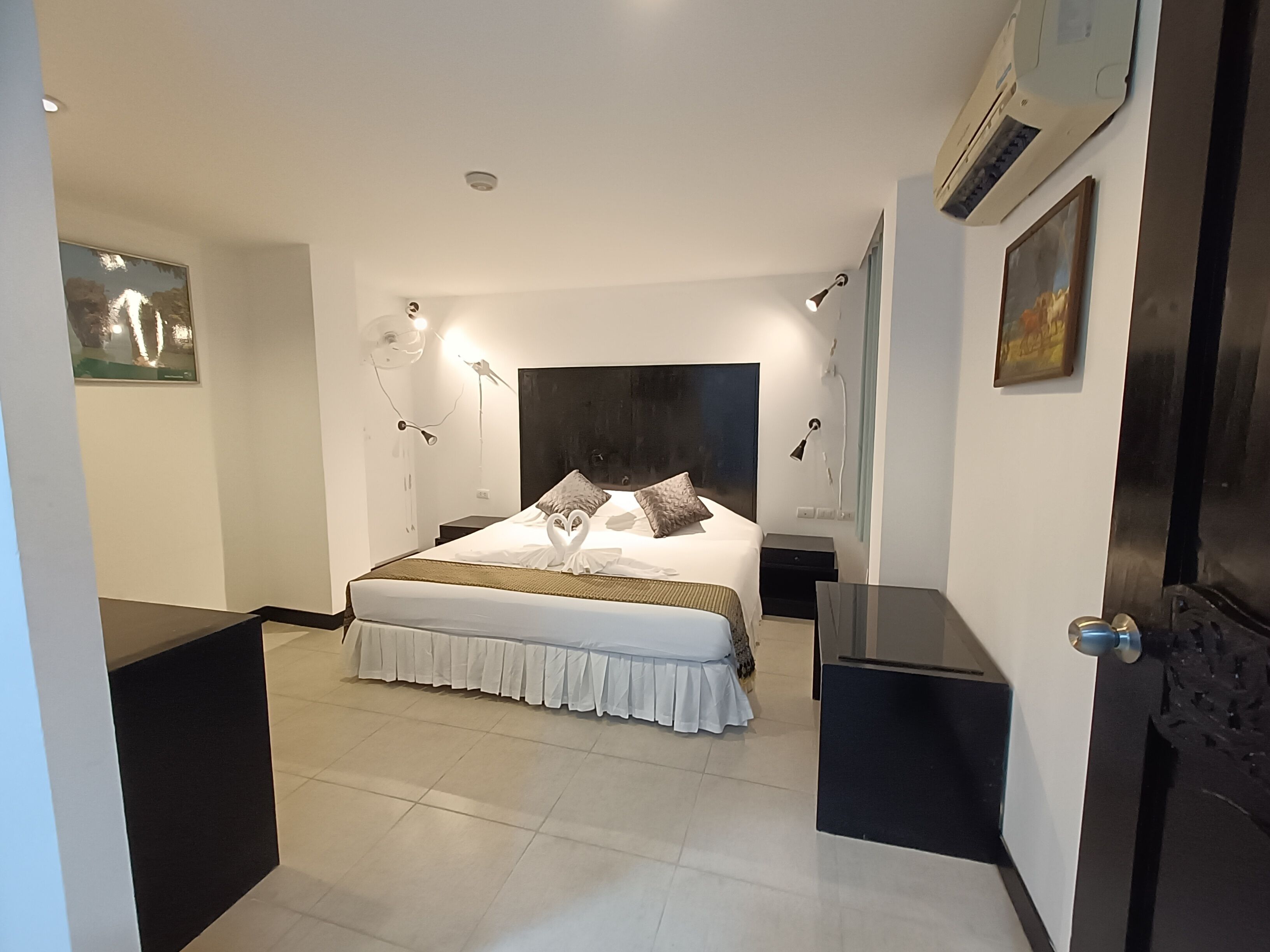 A modern hotel room with a large bed, bedside tables, a desk, and a wall-mounted air conditioner.