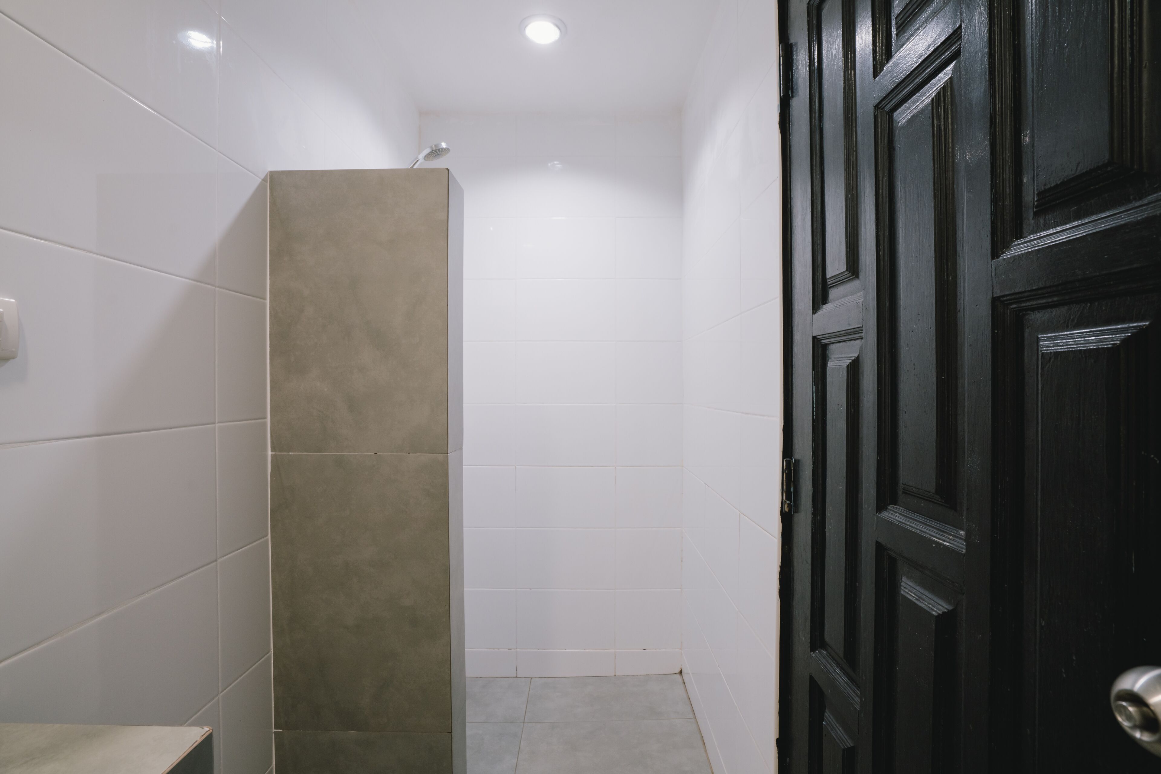 A bathroom with white tiles, a beige accent wall, and a black door.