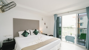 A hotel room with a large bed, a bedside table with a lamp, a nightstand with a phone, and a balcony with a table and chairs.