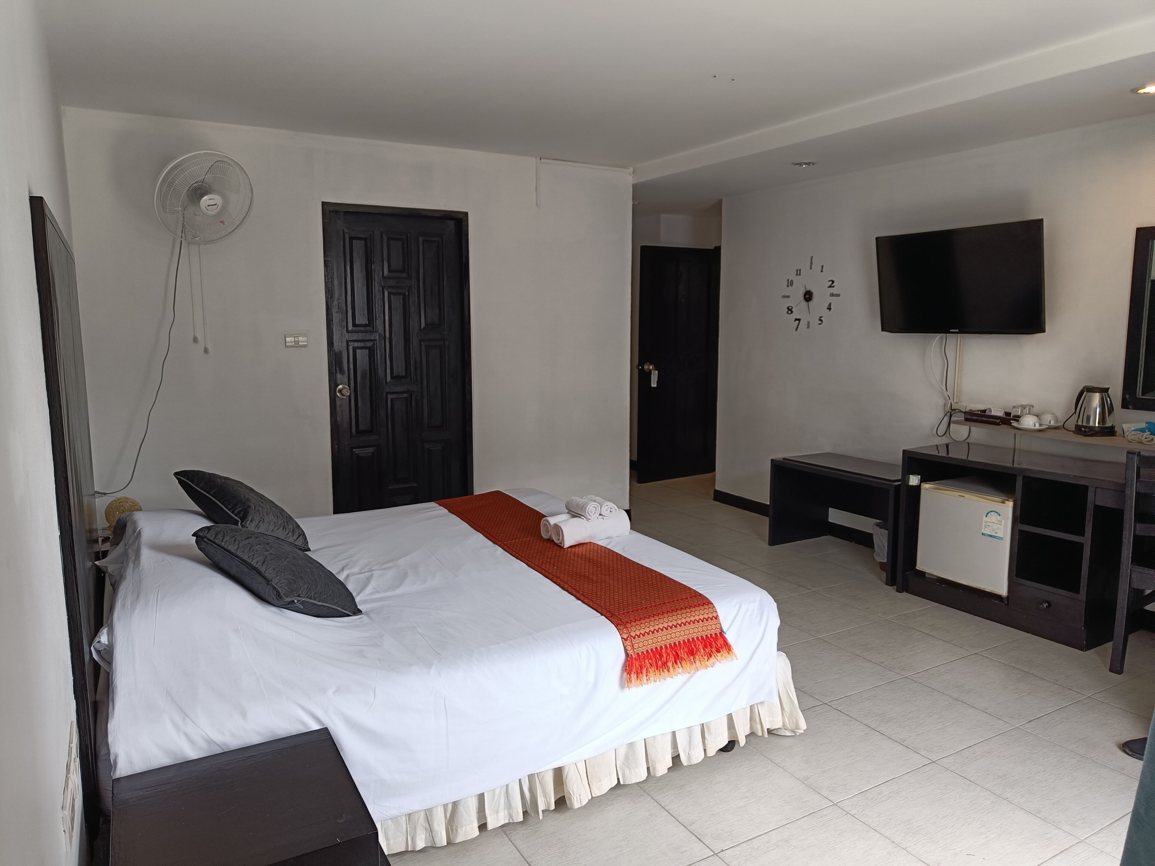A hotel room with a bed, a desk, a chair, a TV, and a door.