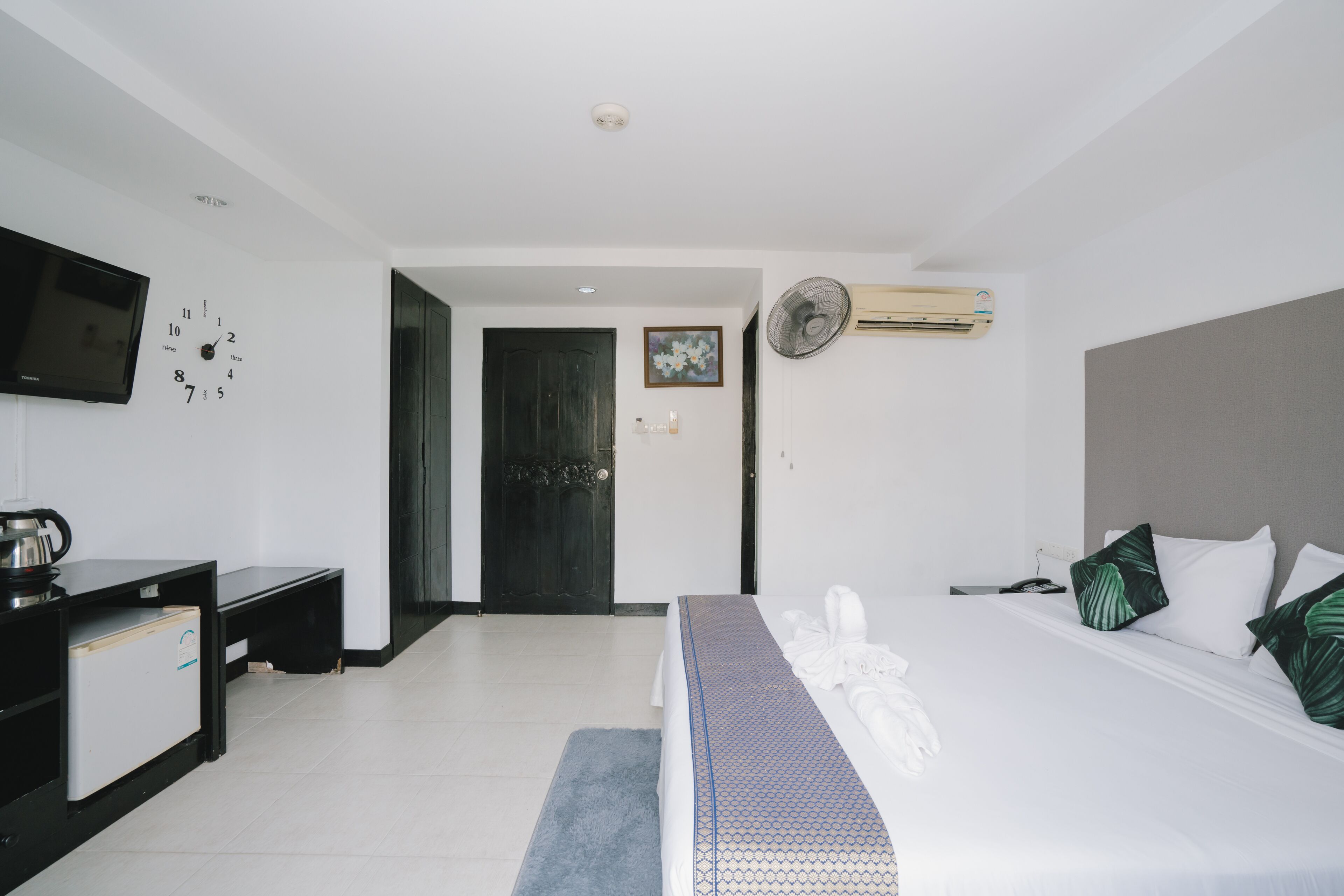 A hotel room with a bed, a TV, a desk, and a door.