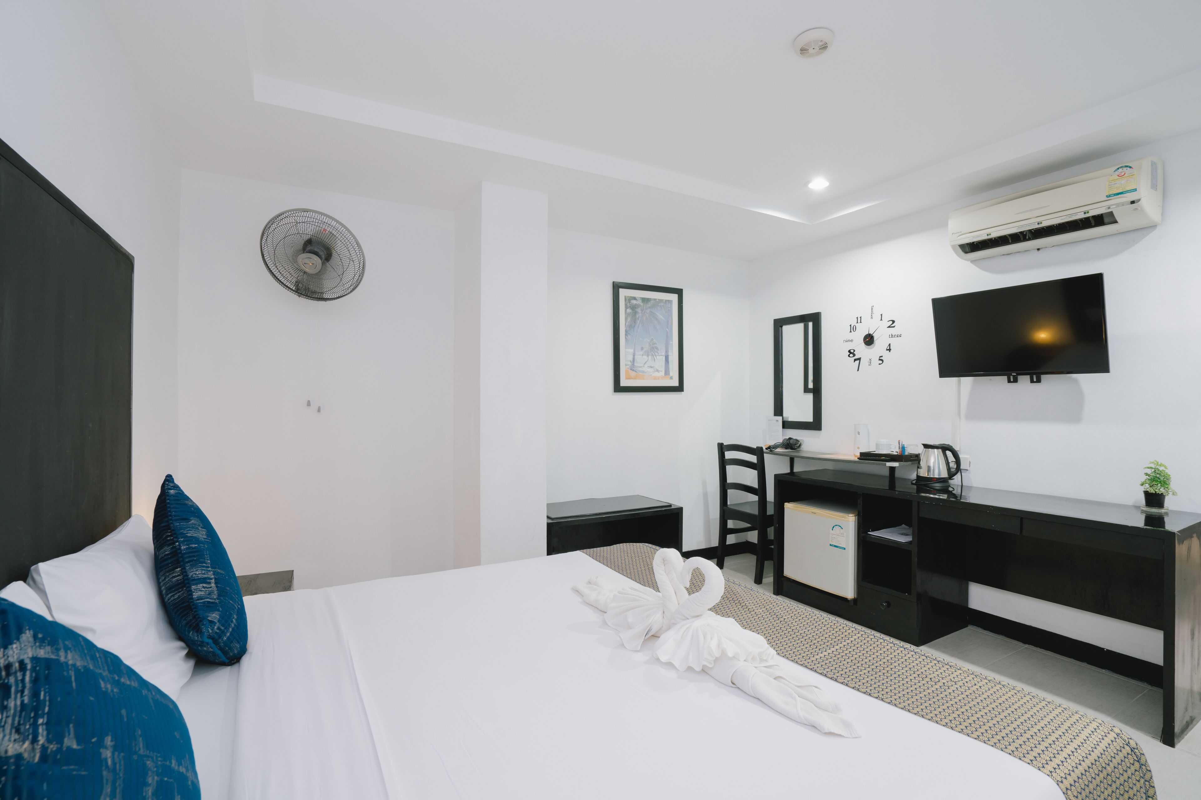A hotel room with a bed, a desk, a chair, a TV, and an air conditioning unit.