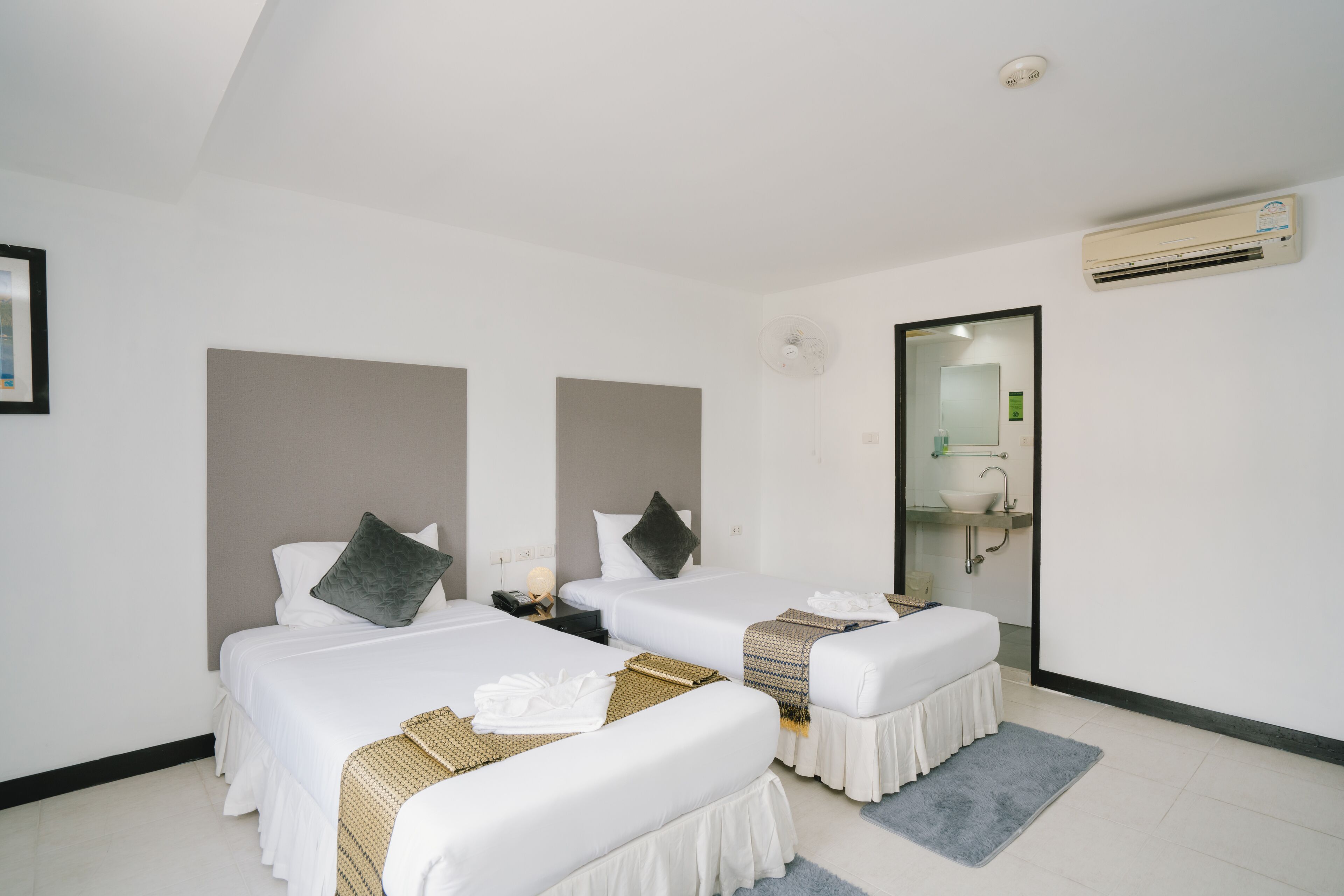 A hotel room with two beds, a bathroom with a sink and mirror, and an air conditioning unit.