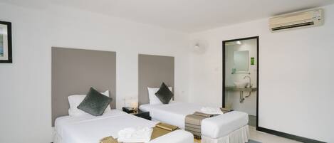 A hotel room with two beds, a bathroom with a sink and mirror, and an air conditioning unit.
