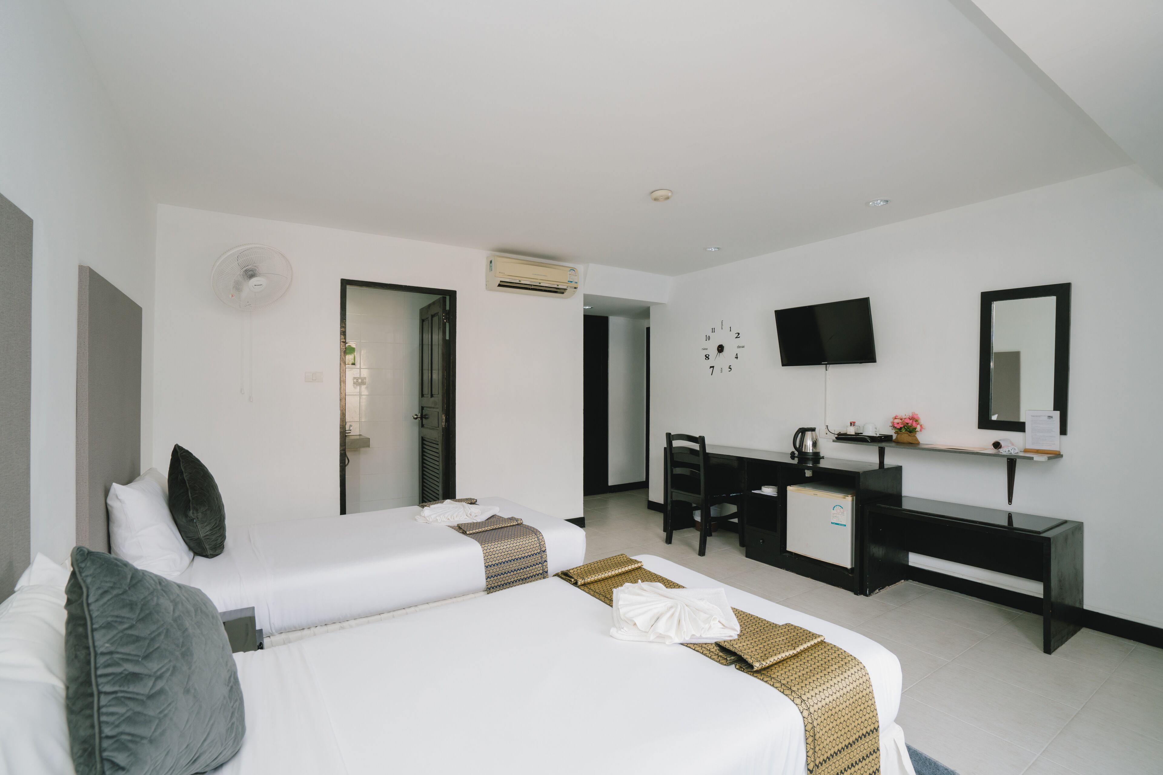 A hotel room with two beds, a desk, a chair, a TV, and a mirror.