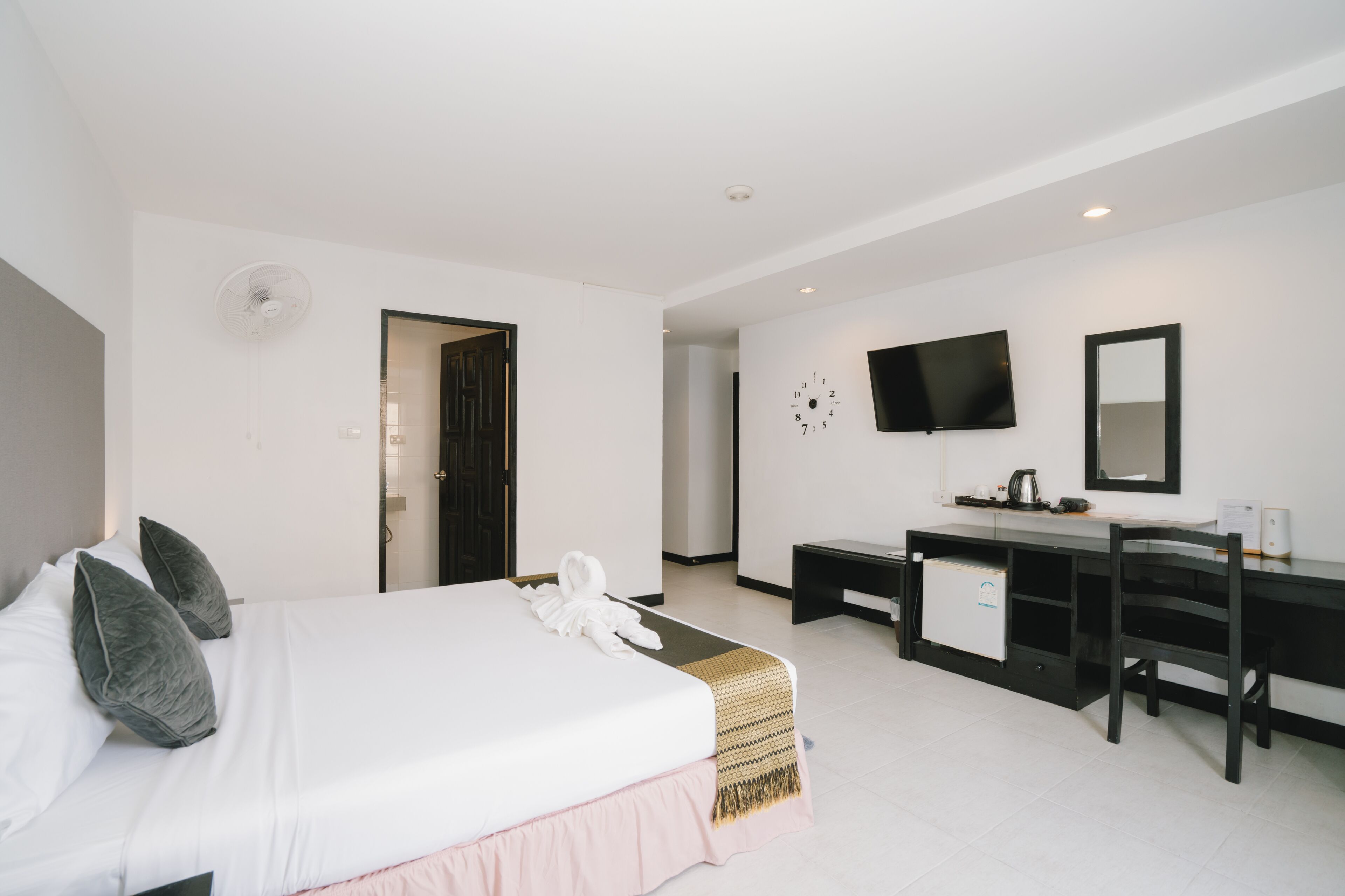 A hotel room with a bed, a desk, a chair, a TV, and a clock on the wall.