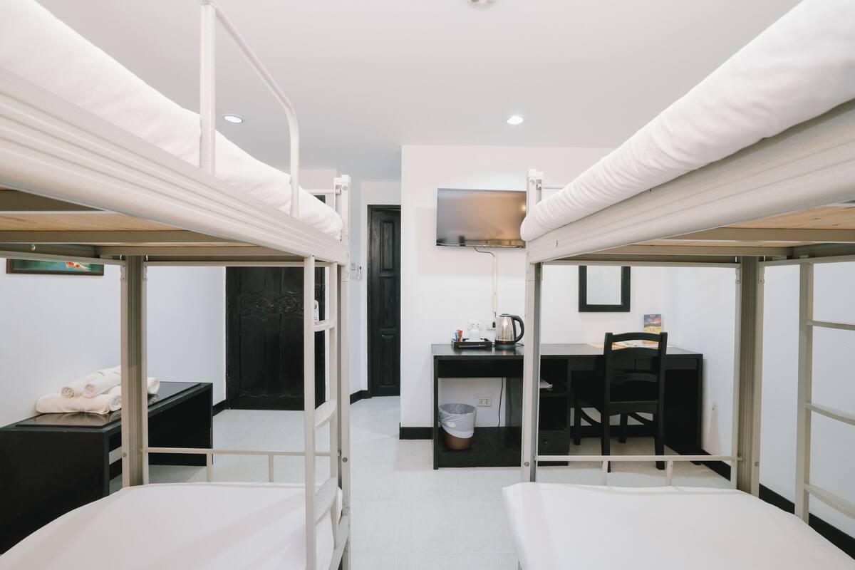 Une chambre de dortoir avec des lits superposés, un bureau, une chaise et un téléviseur fixé au mur.