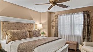 Quarto com uma cama grande, um ventilador de teto, uma mesa de cabeceira com abajur e uma janela com cortinas.