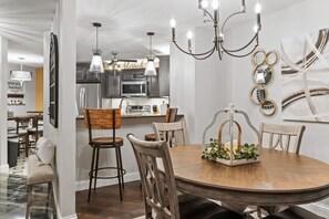 A dining area with a wooden table and chairs, a chandelier, and a kitchen in the background. - Beautiful, Updated Golf Condo near Shows and Attractions (Branson)
