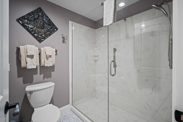 A bathroom with a glass-enclosed shower, a toilet, and a wall-mounted towel rack with towels. - Beautiful, Updated Golf Condo near Shows and Attractions (Branson)