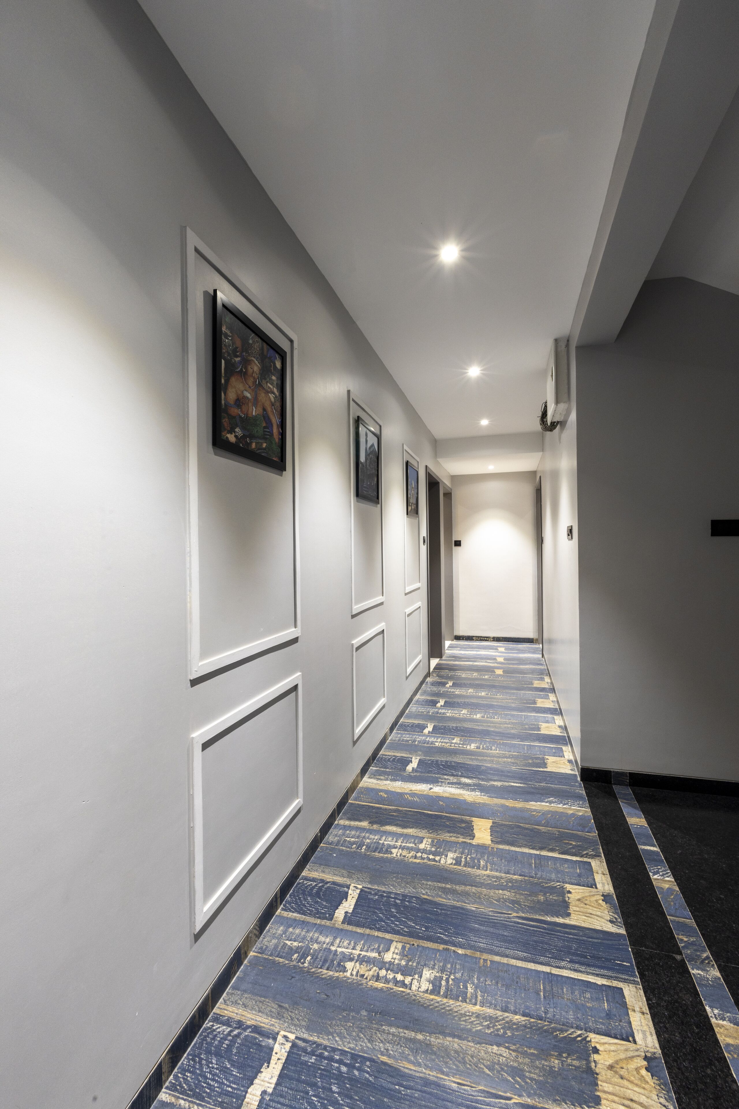 A hallway with a patterned carpet, white walls, and framed artwork.