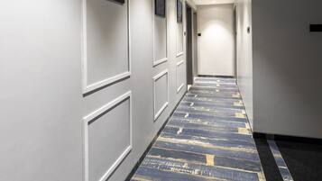 A hallway with a patterned carpet, white walls, and framed artwork.