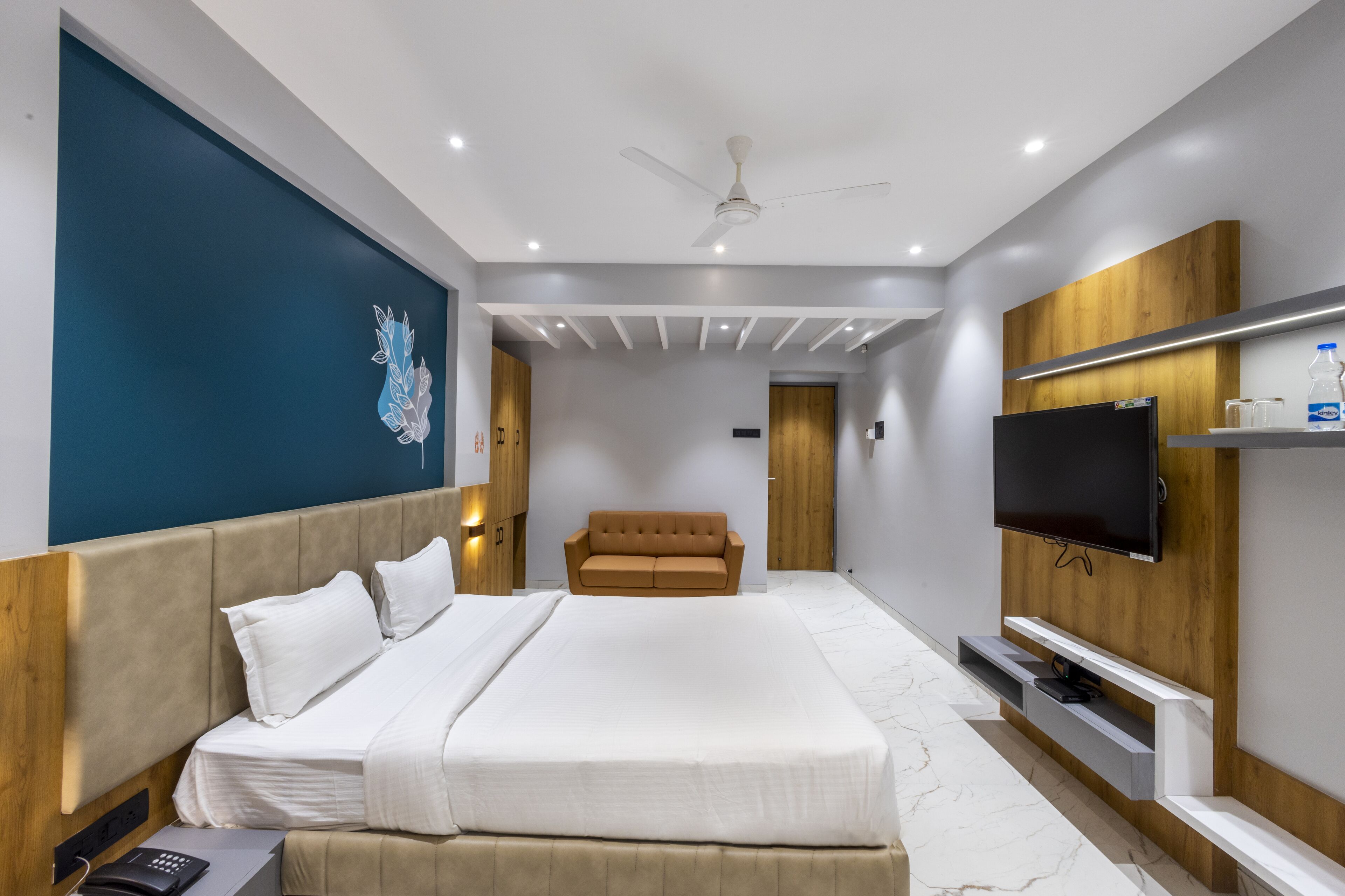 Una habitación de hotel moderna con una cama grande, un televisor de pantalla plana, un ventilador de techo y una pared decorativa de madera.