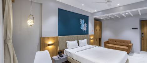 A modern hotel room with a large bed, a seating area, a ceiling fan, and a wall-mounted artwork.