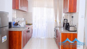 A compact kitchen with wooden cabinets, a refrigerator, a microwave, and a toaster. - George's Fully Furnished 2 Bedroom Apartment (Nairobi)