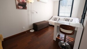 Ein gemütlicher Raum mit Bett, Schreibtisch, Stuhl, Stehlampe und einem Fenster mit Jalousien.