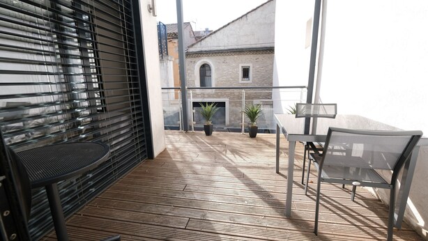 Ein Balkon mit Holzboden, Metallstühlen und Blumentöpfen.