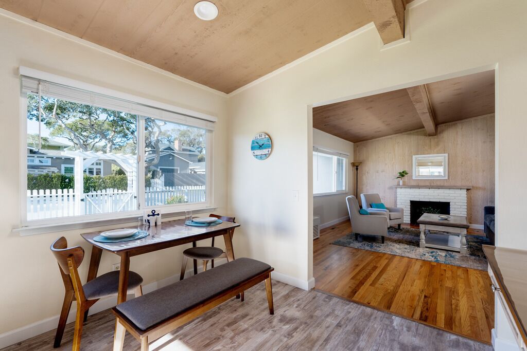 A dining area with a wooden table and chairs, a bench, and a view of the outside through large windows.