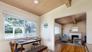 A dining area with a wooden table and chairs, a bench, and a view of the outside through large windows. - Simple Pleasures - Pacific Grove House - America's "Last Hometown" (Pacific Grove)
