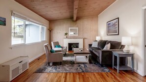 A living room with a fireplace, wooden ceiling, and large windows. - Simple Pleasures - Pacific Grove House - America's "Last Hometown" (Pacific Grove)