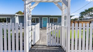 A white wooden pergola with a clear pathway leading to a house with a blue door and windows. - Simple Pleasures - Pacific Grove House - America's "Last Hometown" (Pacific Grove)