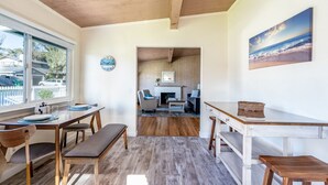 A spacious living area with a wooden ceiling, a dining table with chairs, a bench, and a fireplace. - Simple Pleasures - Pacific Grove House - America's "Last Hometown" (Pacific Grove)