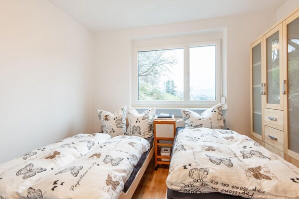 A bedroom with two beds, a window, and a wardrobe.