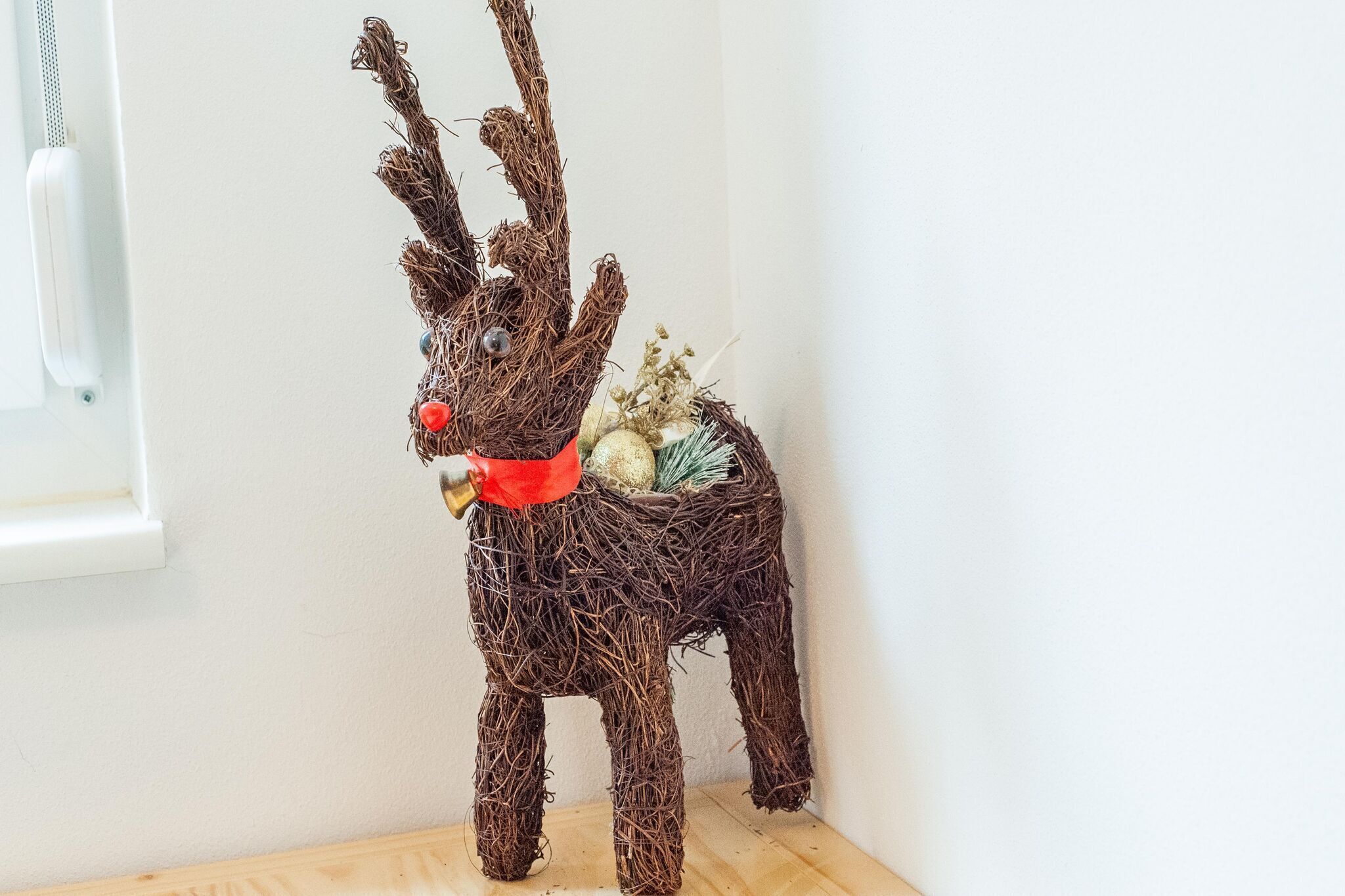 A decorative reindeer sculpture made of twigs, with a red bow and a small nest containing eggs and dried plants.