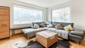 A modern living room with a sectional sofa, a wooden coffee table, and a large window offering a city view. - Holiday Home Feldkirch Panoramic Views (Feldkirch)
