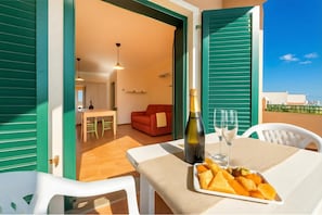 Ein offener Balkon mit Tisch für zwei Personen, einer Champagnerflasche und einer Obstplatte.